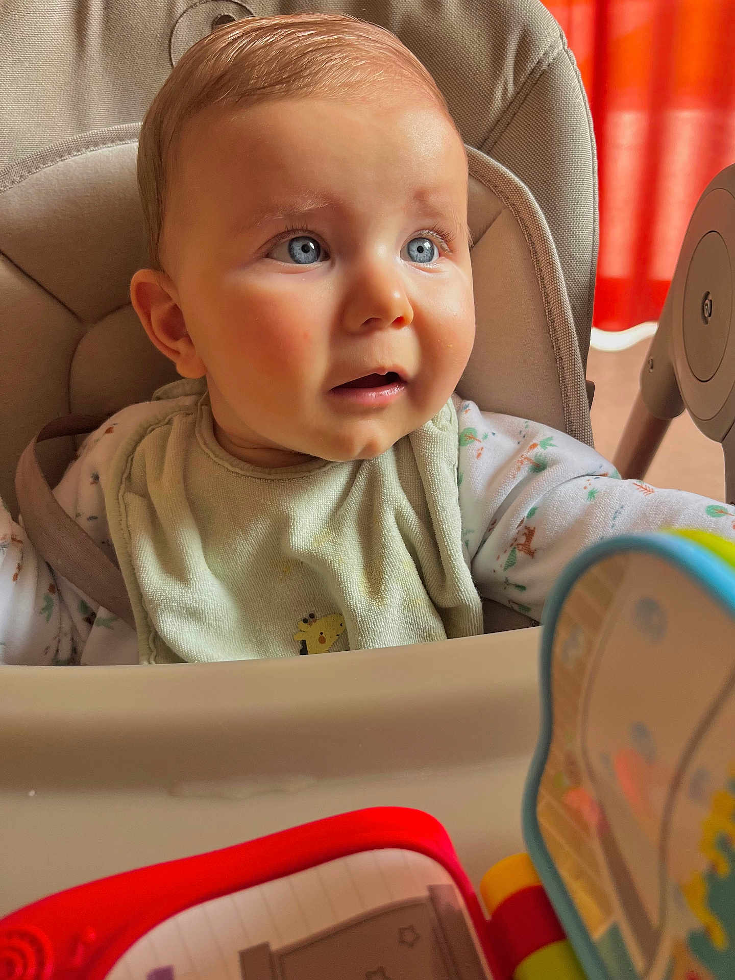 Elio a rejoint le concours — aidez-le/la à gagner de superbes lots ! baby, high_chair, bib, blue_eyes, indoor, toy, curious, child, infant, seated, clothing, face, expression, person, furniture, red_curtain, soft_light, closeup, cute, young_child