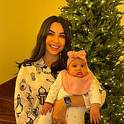 Makayla is registered to the contest to win money with this photo: woman, baby, child, christmas_tree, holiday, smile, indoor, pajamas, headband, lights, celebration, family, holding, festive, cheerful, portrait, warm_lighting, jewelry, watch, stairs
