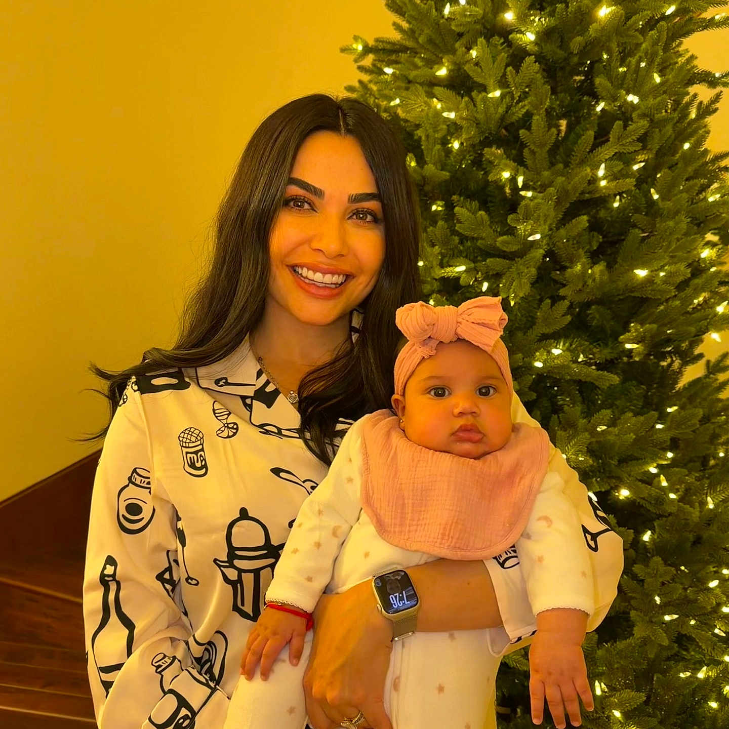 Makayla is registered to the contest to win money with this photo: baby, celebration, cheerful, child, christmas_tree, family, festive, headband, holding, holiday, indoor, jewelry, lights, pajamas, portrait, smile, stairs, warm_lighting, watch, woman