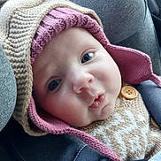 Lynaë a rejoint le concours — aidez-le/la à gagner de superbes lots ! baby, face, closeup, knitted_hat, knitted_sweater, button, seatbelt, car_seat, child, cute, expression, warm_clothing, indoors, infant, portrait, person, headwear, seat, young_child, soft_lighting