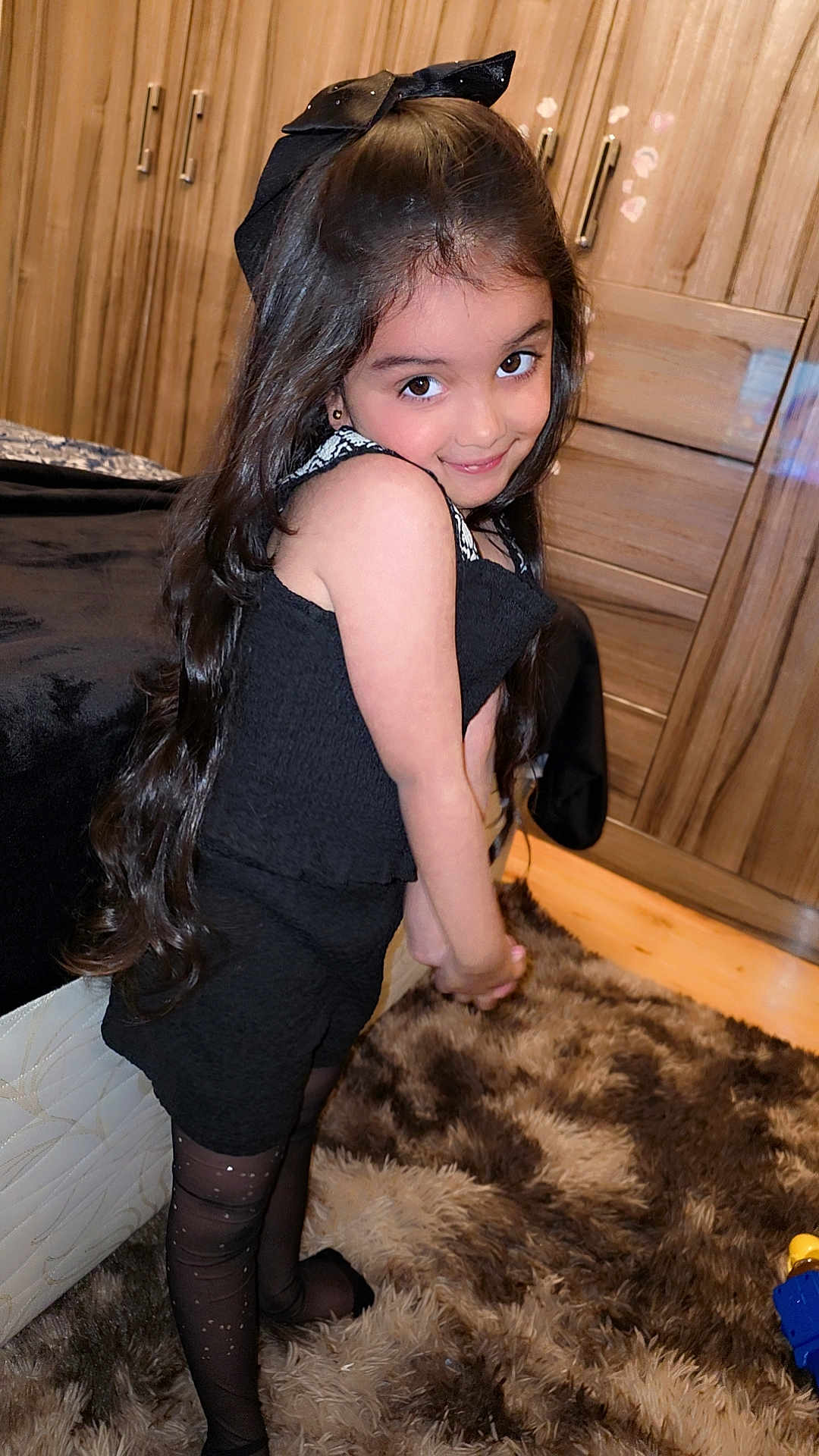 Hajrah joined the competition — help win amazing prizes! child, girl, black_dress, long_hair, bow, smile, indoor, carpet, wooden_cabinet, furniture, posing, cute, portrait, stockings, happy, young, fashion, home, floor, room