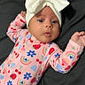 baby, infant, child, portrait, lying_down, bed, bow_headband, pink_outfit, patterned_clothing, strawberries, flowers, rainbows, hearts, wide_eyes, surprised_expression, arms_raised, indoor, close_up, cute, photography
