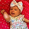 Aurora is registered to the contest to win money with this photo: baby, infant, child, smiling, happy, lying_down, portrait, face, floral_outfit, hair_bow, red_blanket, polka_dots, indoor, close_up, baby_fashion, bracelet, raised_arm, colorful, cute, photography