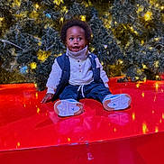 Jaylon a rejoint le concours — aidez-le/la à gagner de superbes lots ! child, christmas_tree, cute, decorations, happy, holiday_lights, indoor, jeans, ornament, pine_branches, portrait, red_platform, reflection, scarf, seasonal, sitting, smile, sneakers, toddler, vest