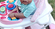 Deannalee is registered to the contest to win money with this photo: baby, walker, grass, outdoor, child, toy, pink, blue, hair_clip, curly_hair, person, seat, wheel, playful, cute, infant, hands, foot, summer, daylight