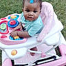 baby, walker, grass, outdoor, child, toy, pink, blue, hair_clip, curly_hair, person, seat, wheel, playful, cute, infant, hands, foot, summer, daylight