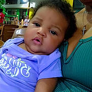 Deannalee is registered to the contest to win money with this photo: baby, infant, child, person, indoor, adult, clothing, purple_shirt, green_top, necklace, cross, face, expression, seated, furniture, lighting, people, background, portrait, closeup