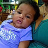 baby, infant, child, person, indoor, adult, clothing, purple_shirt, green_top, necklace, cross, face, expression, seated, furniture, lighting, people, background, portrait, closeup