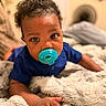 baby, child, infant, pacifier, curly_hair, blue_shirt, portrait, close_up, smiling, face, eyes, bedroom, bed, blanket, bedding, cozy, indoor, sitting, crawling, photography