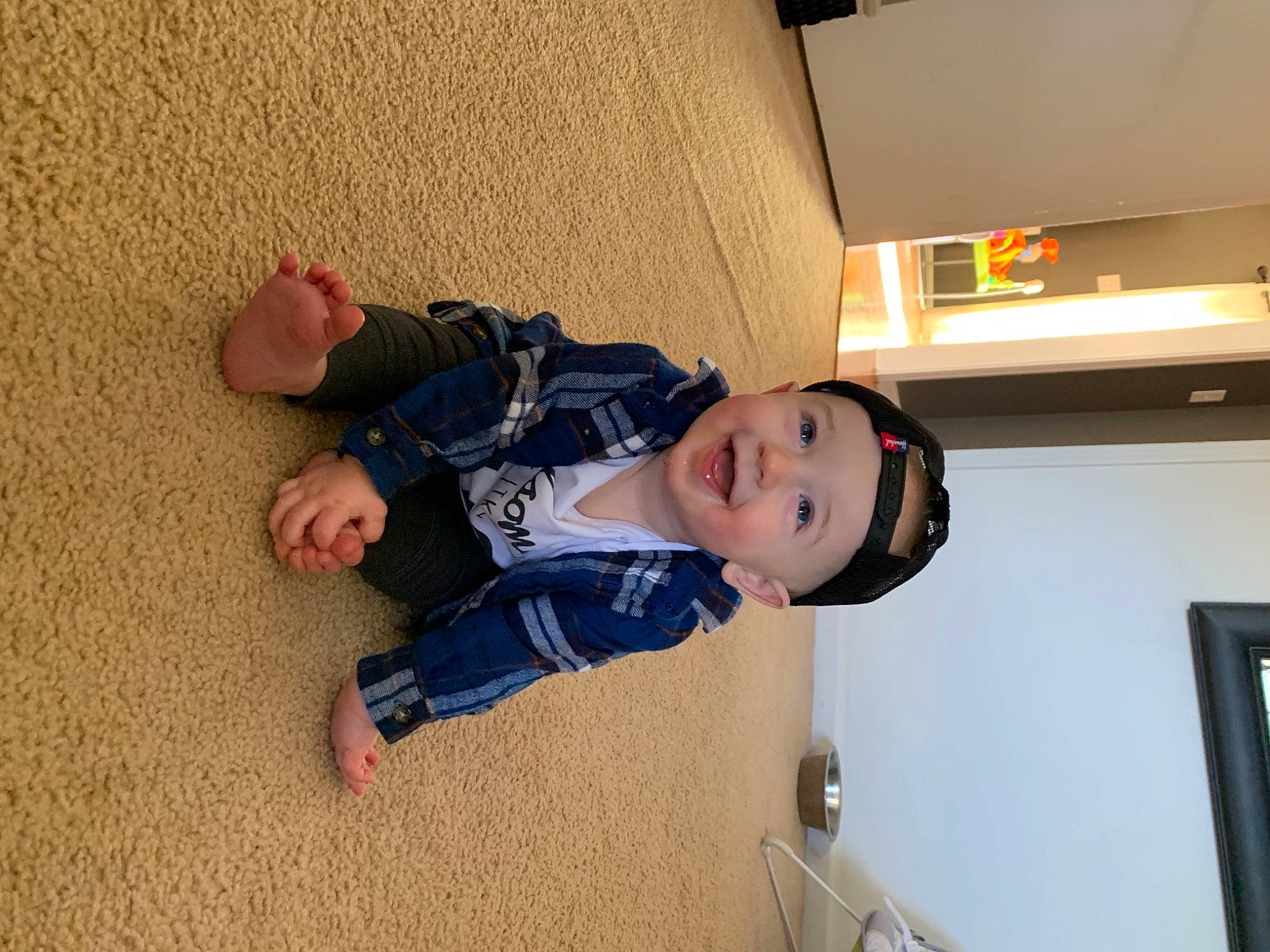 Grey is registered to the contest to win money with this photo: baby, baby_toddler_clothing, child, comfort, floor, flooring, foot, fun, happy, hat, headwear, human_leg, jacket, joy, person, room, sitting, smile, standing, toddler