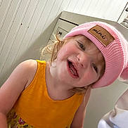 Ruby joined the competition — help win amazing prizes! toddler, child, pink_hat, yellow_dress, smiling, indoor, cabinet, face, person, cute, happy, portrait, headwear, clothing, skin, hair, expression, baby, room, playful