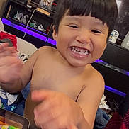Liam Rivera is registered to the contest to win money with this photo: child, toddler, smiling, laughing, happy, portrait, indoors, home, sitting, waving, hands, short_hair, bangs, bare_shoulders, clothing, toy, tablet, television, led_lights, furniture