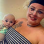 baby, woman, glasses, headband, striped_clothing, tattoo, necklace, smile, indoor, portrait, person, child, holding, face, skin, young, casual, light, happy, background