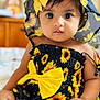 baby, child, sunflower, hat, yellow_bow, dress, cute, portrait, indoors, sitting, infant, face, eyes, skin, hand, clothing, headwear, patterned_clothing, closeup, adorable