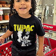 Michael joined the competition — help win amazing prizes! child, toddler, smiling, curly_hair, portrait, standing, shopping_cart, grocery_store, supermarket, retail, indoor, shelves, groceries, red_cart, black_clothing, graphic_t_shirt, tupac_shirt, store_lighting, happy, shopping