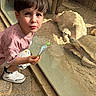 child, boy, tortoise, glass_enclosure, snack, curious, sunlight, shadow, stone_floor, reptile, animal, crouching, casual_clothing, white_shoes, shorts, pink_shirt, indoor, zoo, observation, daylight