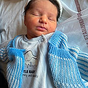 Lùcia a rejoint le concours — aidez-le/la à gagner de superbes lots ! newborn, baby, sleeping, infant, knitted_cardigan, blue, white, onesie, elephant_graphic, text_on_clothing, soft_blanket, peaceful, cute, portrait, closeup, headband, clothing, indoors, child, resting