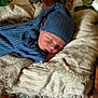 baby, sleeping, blue_outfit, knit_hat, blanket, newborn, soft_texture, flowers, greenery, wooden_surface, peaceful, cozy, infant, portrait, resting, cute, child, closeup, warm_colors, indoor
