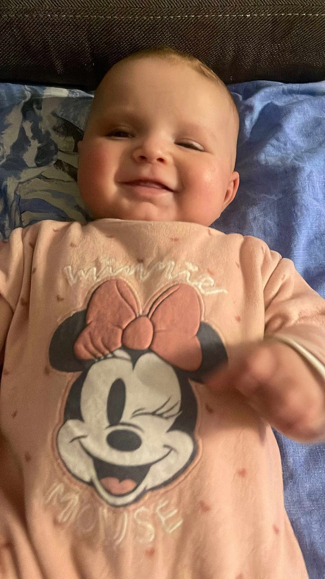 Amina participe au concours pour gagner de l'argent avec cette photo : baby, child, smile, face, pink_clothing, minnie_mouse, cartoon_character, blanket, lying_down, infant, cute, winking, indoor, soft_lighting, portrait, happy, young_child, cozy, apparel, person