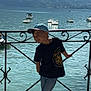 boy, child, cap, tshirt, jeans, shoes, lake, water, boats, mountains, railing, smile, outdoor, sunlight, scenic, casual, daylight, nature, person, happy