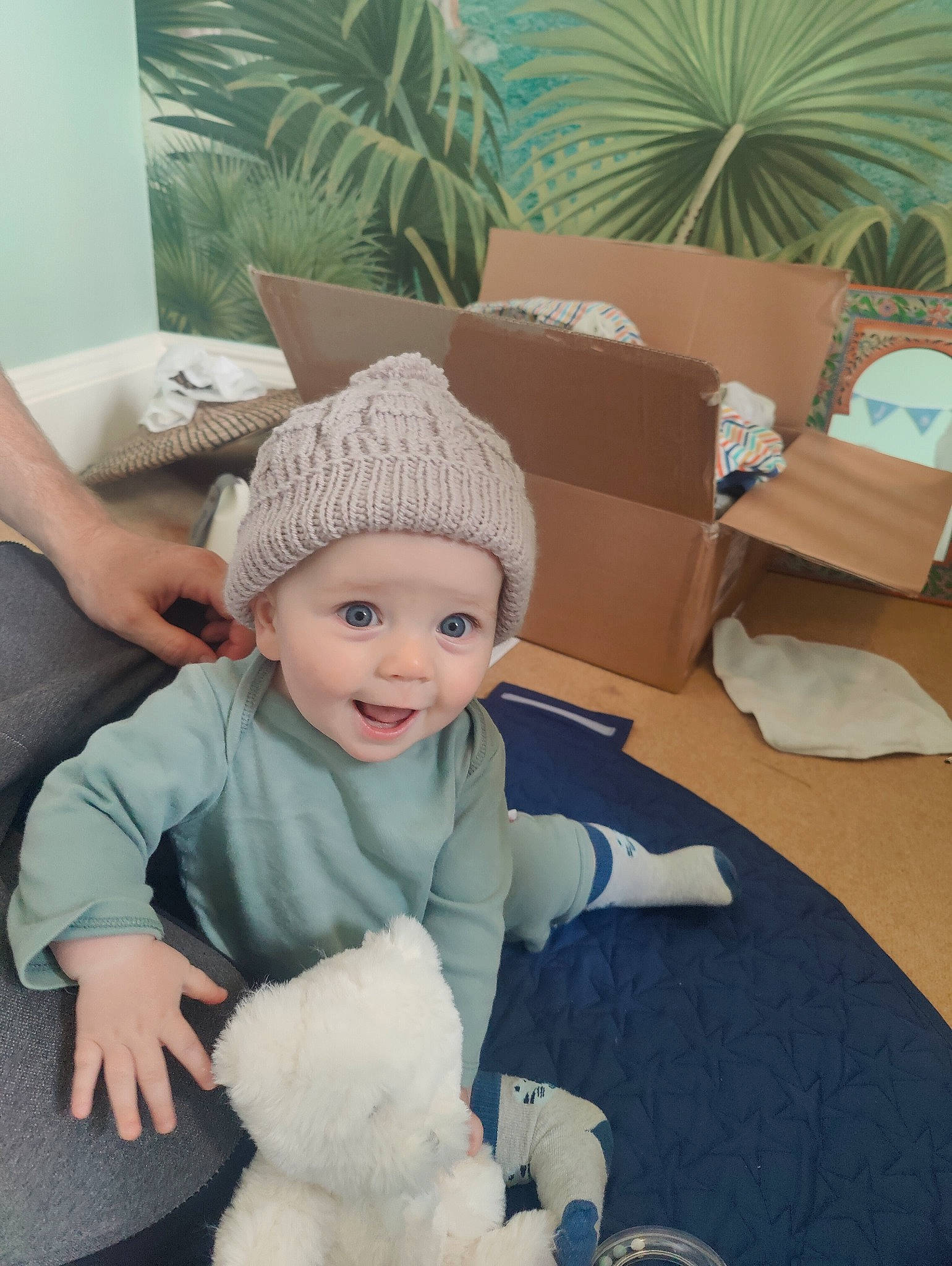 Caelan joined the competition — help win amazing prizes! baby, baby_toddler_clothing, beanie, cap, child, comfort, flooring, grass, happy, headwear, houseplant, knit_cap, linens, mammal, person, plant, room, sitting, smile, toddler