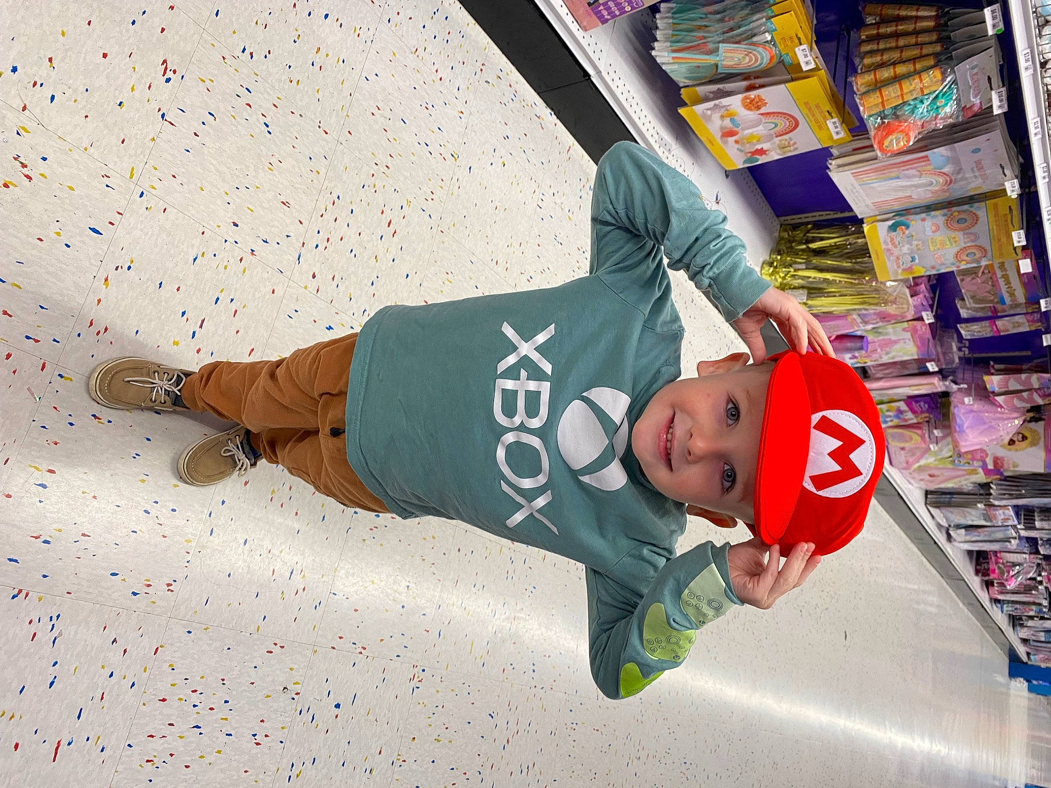 Collin is registered to the contest to win money with this photo: baseball_cap, bookcase, cap, child, fun, hat, headwear, joy, leisure, logo, person, publication, retail, shelf, shopping, sleeve, smile, street, sunglasses, t_shirt