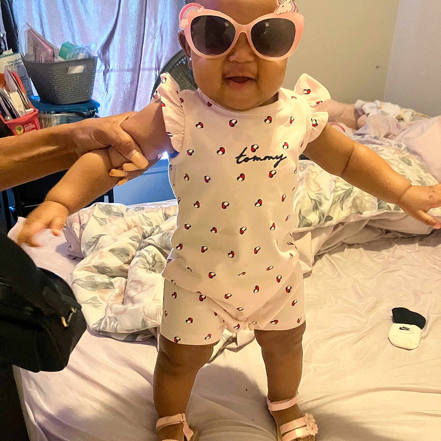 Sarya is registered to the contest to win money with this photo: accessory, bed, blanket, child, clothing, curtain, cute, footwear, hand, happy, home, indoor, person, pink, smile, standing, sunglasses, support, toddler, window