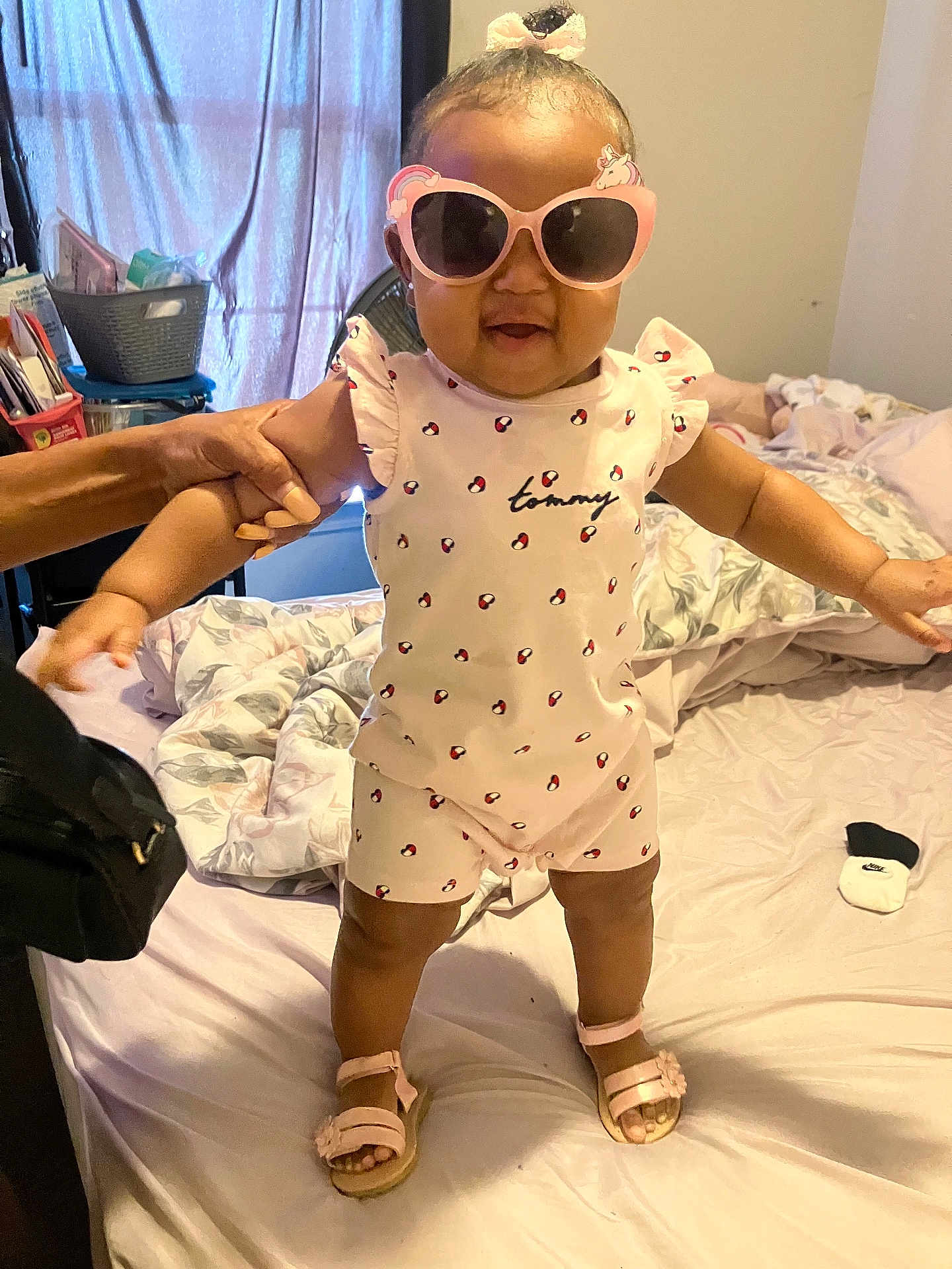 Sarya is registered to the contest to win money with this photo: toddler, child, sunglasses, pink, standing, bed, hand, support, clothing, footwear, indoor, blanket, window, curtain, person, smile, happy, home, cute, accessory