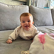 Gabriel participe au concours pour gagner de l'argent avec cette photo : baby, child, couch, cute, face, furniture, gray_sofa, happy, home, indoor, infant, living_room, pacifier, person, pillow, pink_feather, relaxed, smiling, sweater, young_child