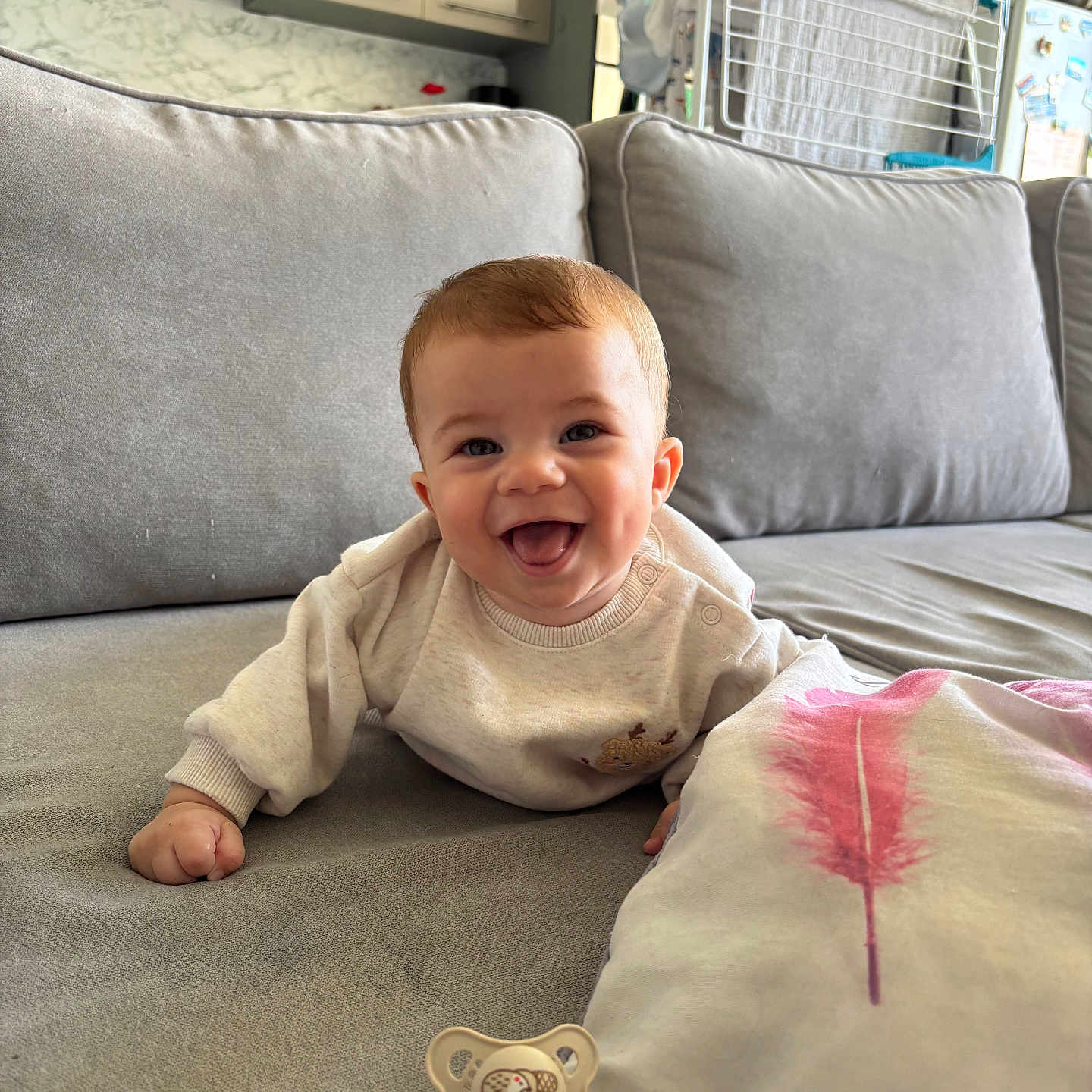 Gabriel participe au concours pour gagner de l'argent avec cette photo : baby, child, couch, cute, face, furniture, gray_sofa, happy, home, indoor, infant, living_room, pacifier, person, pillow, pink_feather, relaxed, smiling, sweater, young_child