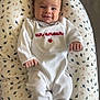 baby, infant, smiling, onesie, white_clothing, cushion, bird_pattern, soft_furniture, indoor, child, portrait, cute, happy, lying_down, cozy, small_hands, head, face, blue_eyes, toddler