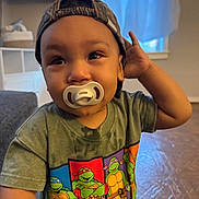 Callen joined the competition — help win amazing prizes! toddler, child, pacifier, hat, cap, camouflage, shirt, teenage_mutant_ninja_turtles, green_shirt, indoor, person, hand, floor, window, curtains, furniture, face, expression, young_child, casual_clothing