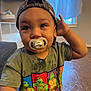 toddler, child, pacifier, hat, cap, camouflage, shirt, teenage_mutant_ninja_turtles, green_shirt, indoor, person, hand, floor, window, curtains, furniture, face, expression, young_child, casual_clothing