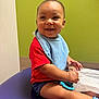 Callen is registered to the contest to win money with this photo: baby, child, smile, red_shirt, blue_bib, toy, drool, sitting, purple_surface, green_wall, shorts, happy, indoor, skin, hand, face, head, person, infant, cute