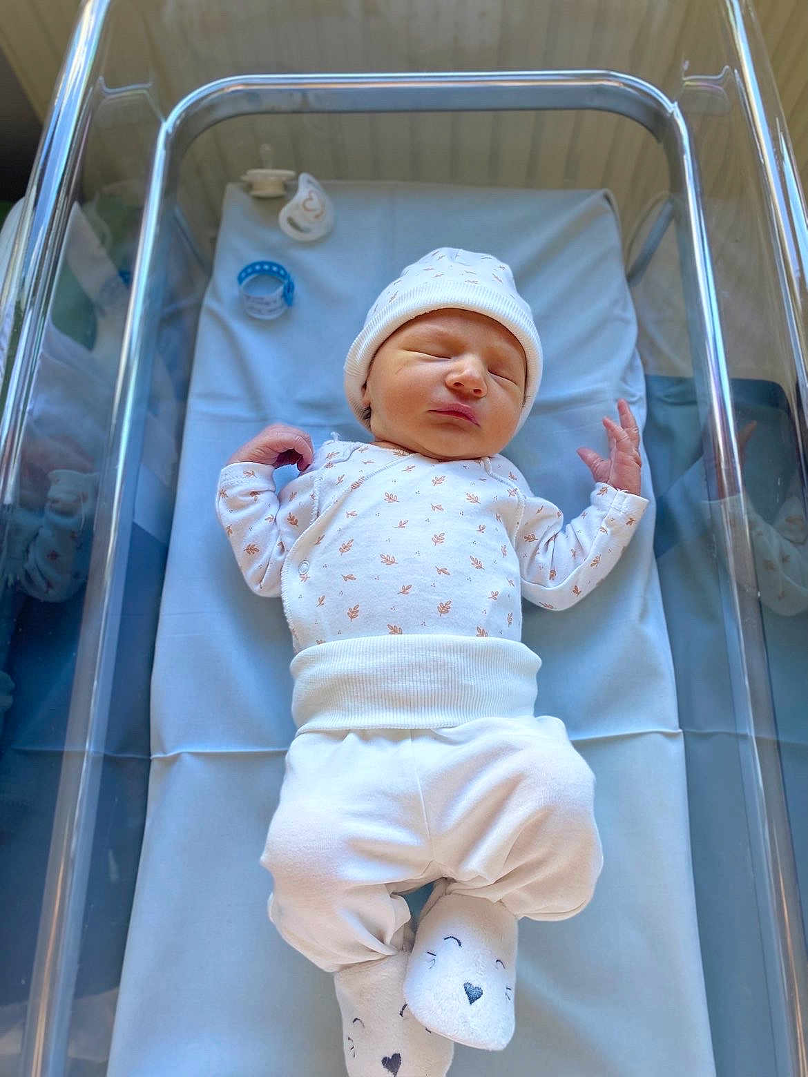 Elyo a rejoint le concours — aidez-le/la à gagner de superbes lots ! newborn, baby, sleeping, infant, hospital, bassinet, white_clothing, hat, socks, pacifier, blue_bedding, peaceful, cute, tiny_hands, soft_light, indoors, portrait, person, resting, cozy