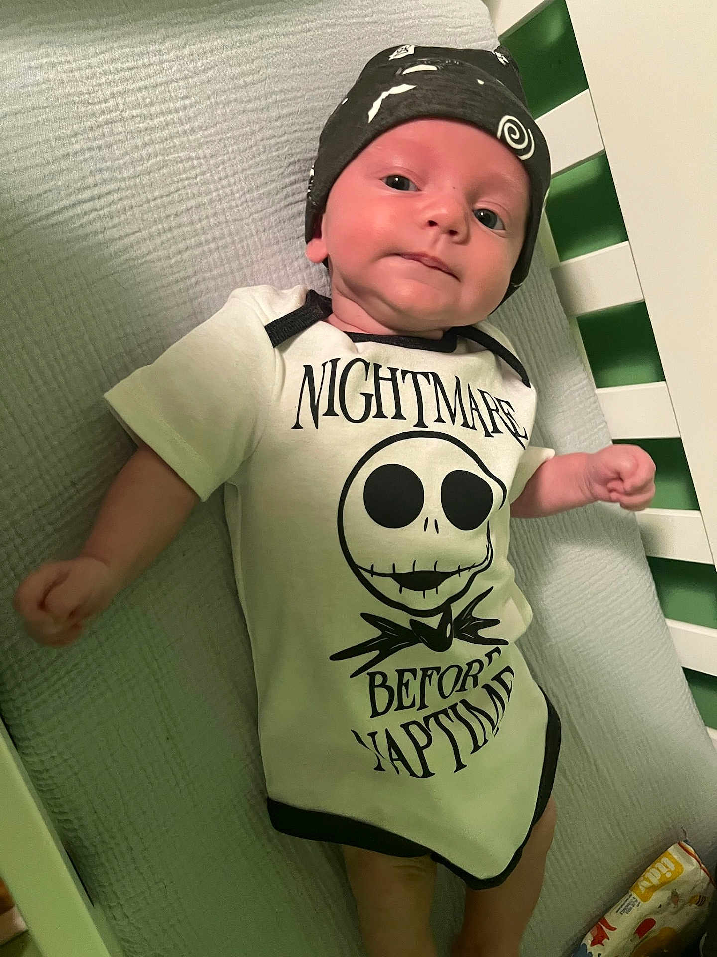 Waylon Hood joined the competition — help win amazing prizes! baby, infant, crib, onesie, hat, face, person, clothing, bed, sleepwear, cute, expression, child, newborn, smile, indoors, text_on_clothing, blanket, rest, naptime