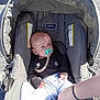 baby, pacifier, car_seat, evenflo, clothing, socks, hand, person, infant, outdoor, sunlight, asphalt, gray, comfort, baby_clothes, bracelet, footwear, toy_clip, seat, portrait