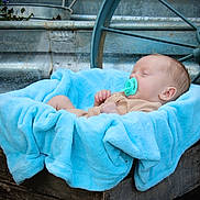 Waylon Hood is registered to the contest to win money with this photo: baby, blanket, wooden_crate, pacifier, sleeping, blue, soft_texture, vintage, wagon_wheel, metal, rustic, outdoor, infant, peaceful, cute, portrait, child, resting, cozy, background