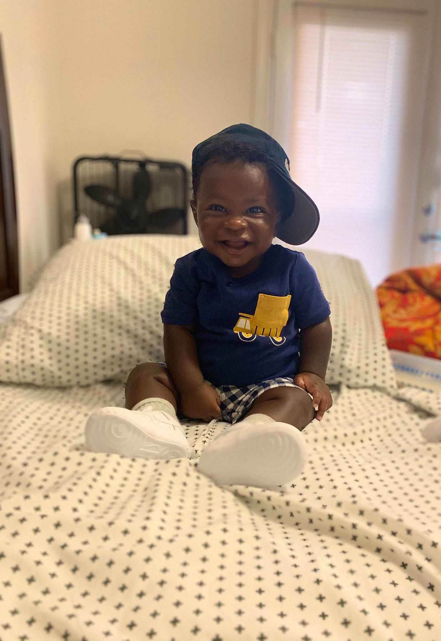 Tahj joined the competition — help win amazing prizes! bedding, bedroom, cap, carpet, child, comfort, floor, flooring, fun, happy, hardwood, hat, linens, pattern, person, room, sitting, smile, t_shirt, toddler