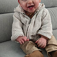 Amaël a rejoint le concours — aidez-le/la à gagner de superbes lots ! baby, child, smiling, sitting, couch, clothing, knitted_jacket, brown_socks, happy, indoor, person, cute, portrait, face, young_child, casual, cozy, warm_clothing, infant, comfortable