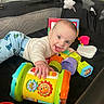 Owen is registered to the contest to win money with this photo: baby, toy, playpen, smiling, colorful, infant, clothing, hand, face, blue_pants, dinosaur_print, star_toy, indoor, happy, child, play, cushion, plastic_toy, person, cute