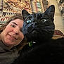 woman, cat, black_cat, face, pet, indoor, selfie, tapestry, curtain, furniture, pattern, close_up, whiskers, collar, home, portrait, expression, looking, cozy, casual