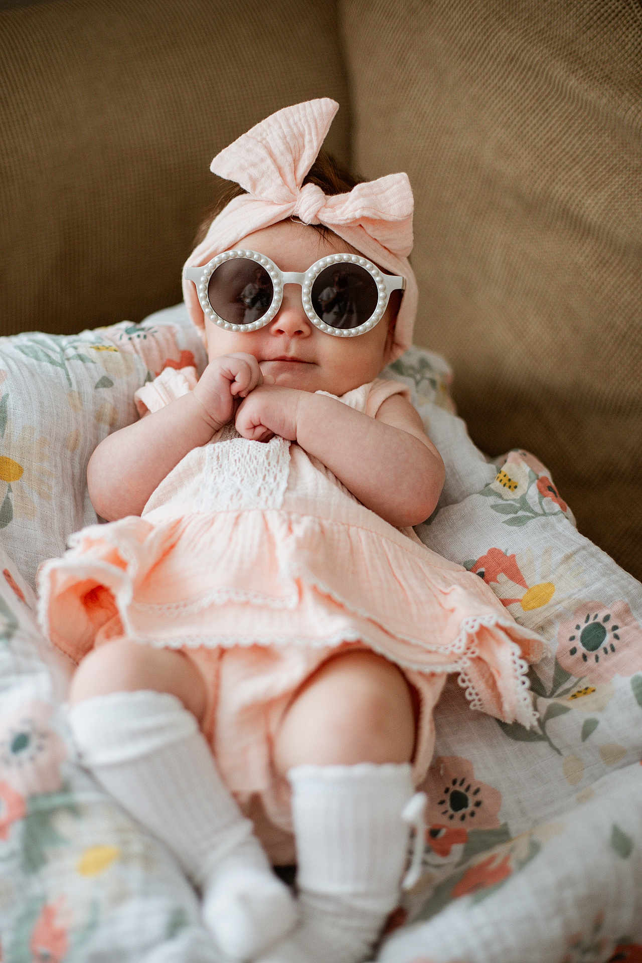 Amelia is registered to the contest to win money with this photo: baby, infant, sunglasses, headband, bow, blanket, floral_pattern, sitting, cute, fashion, clothing, white_socks, soft_lighting, portrait, indoor, couch, smile, hands, legs, skin