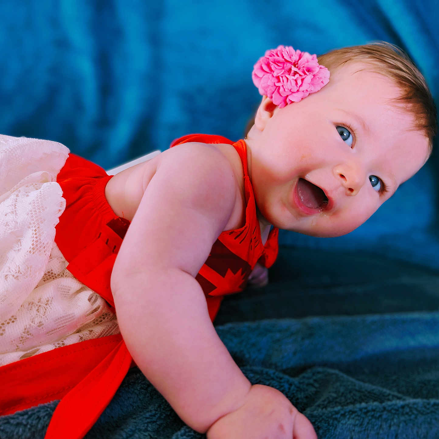 Lily-Rose participe au concours pour gagner de l'argent avec cette photo : baby, blanket, blue_eyes, cheerful, child, cute, flower_headband, hand, happy, head, indoors, infant, lace, lying_down, playful, portrait, red_dress, skin, smiling, soft_texture