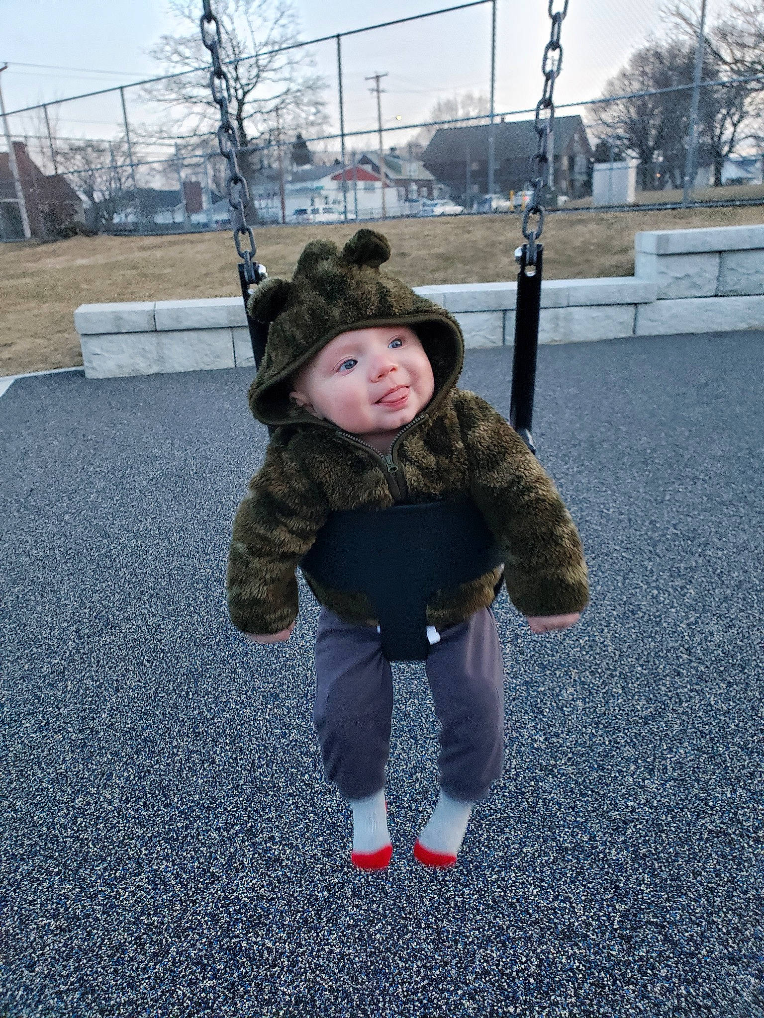 Keith is registered to the contest to win money with this photo: child, city, facial_expression, fun, fur, headwear, jacket, outdoor_play_equipment, people, person, photography, playground, public_space, recreation, skin, smile, snapshot, standing, swing, toddler