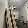 cat, white_cat, mattress, hallway, ceiling_light, wall, door, home_sign, indoor, curious, pet, feline, looking_down, vertical_object, texture, narrow_space, cozy, animal, domestic, playful