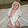 baby, child, clothing, cute, diaper, expression, feet, hand, hood, indoors, infant, laying, medical_table, person, portrait, relaxing, robe, skin, toddler, young