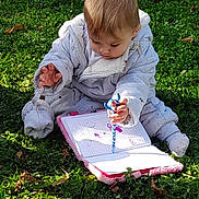 Inaya a rejoint le concours — aidez-le/la à gagner de superbes lots ! toddler, child, grass, notebook, pen, scribbling, outdoor, greenery, clothing, cute, baby, sitting, sunlight, nature, playful, writing, concentration, casual, young, park