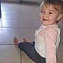 Inaya participe au concours pour gagner de l'argent avec cette photo : toddler, child, smiling, sitting, floor, tile_floor, indoor, clothing, long_sleeve, pants, barefoot, radiator, laundry, window, light, happy, person, young_child, playful, casual