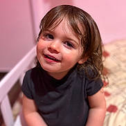 Elya participe au concours pour gagner de l'argent avec cette photo : child, toddler, smile, portrait, face, eyes, hair, black_shirt, bed, blanket, pink_wall, indoor, sitting, close_up, happy, cute, bokeh, skin, young_child, home